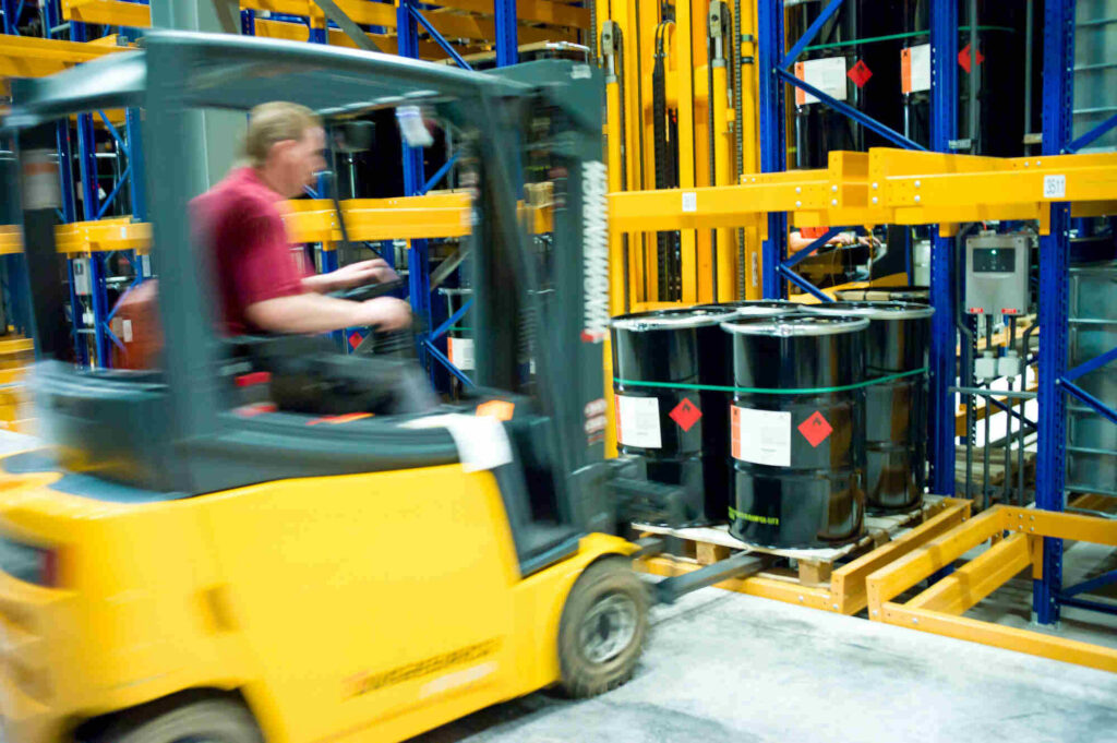 Gefahrguttransport vorbereiten: Stapler bewegt Fässer mit Gefahrzetteln auf einer Palette
