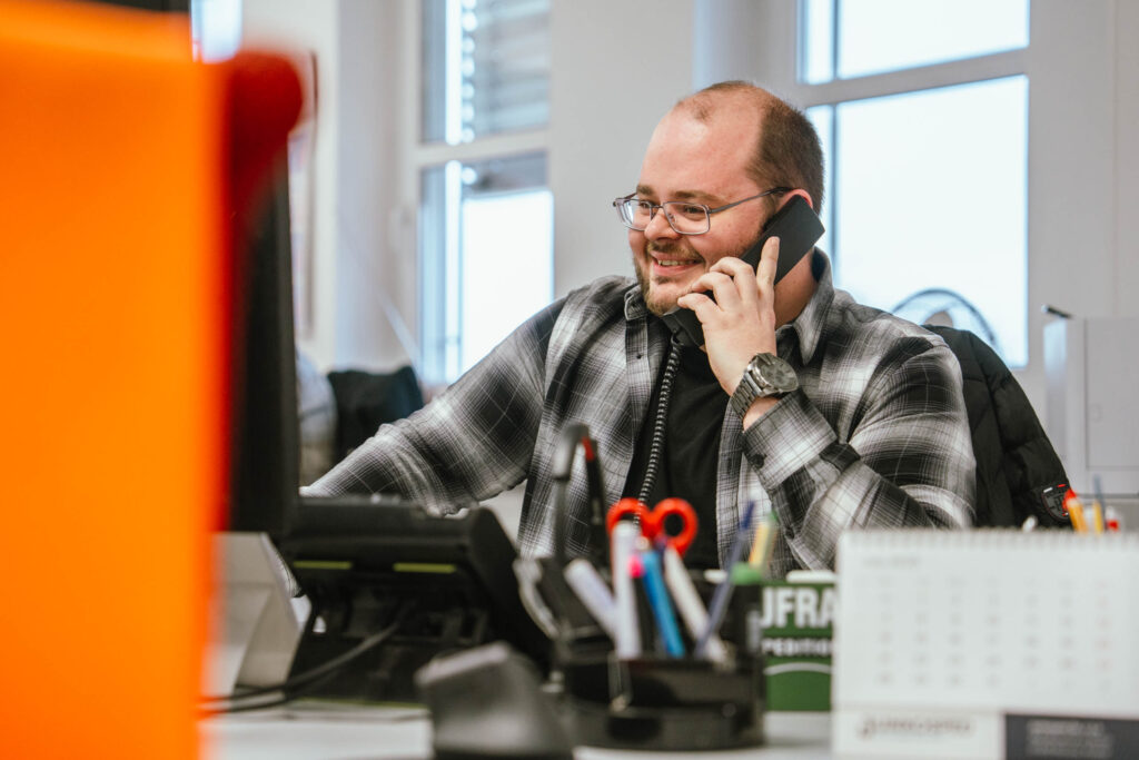 Mitarbeiter der Spedition Mäuler telefoniert lächelnd an seinem Schreibtisch