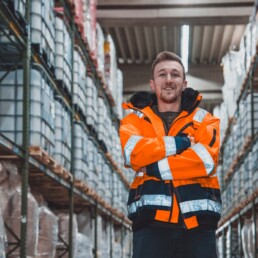 Spedition Mäuler Lagermitarbeiter in Warnschutzjacke zwischen den Regalen im Lager der Spedition Mäuler