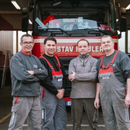 Spedition Mäuler Vier Mitarbeiter der Mäuler-Werkstatt vor einem roten Gustav-Mäuler-Lkw